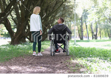 Man in wheelchair is walking in park with his girlfriend Man in wheelchair is walking in park with his girlfriend 81889839