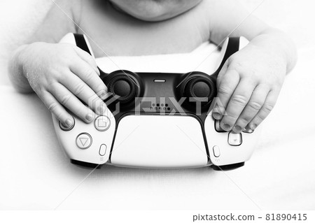 a newborn baby is holding a playstation. fingers of the hands of a newborn. black and white studio photography. a newborn baby is holding a playstation. fingers of the hands of a newborn. black and white studio photography. 81890415