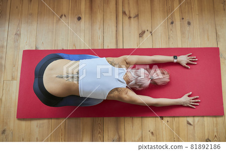 Lady with large tattoo in tracksuit does balasana on wooden floor 81892186