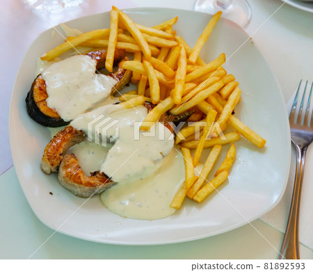 Tasty fried salmon with white sauce and french fries potatoes on plate 81892593