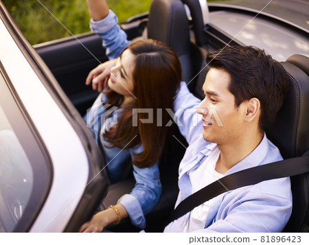 young asian couple riding in a convertible sport car at sunset, high angle view 81896423