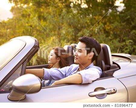 young asian couple riding in a convertible sport car at sunset young asian couple riding in a convertible sport car at sunset 81896477