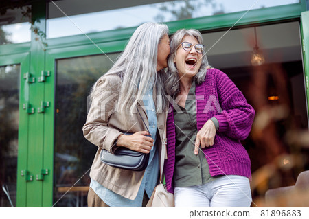 Joyful senior women friends with natural grey hair have fun on city street Joyful senior women friends with natural grey hair have fun on city street 81896883