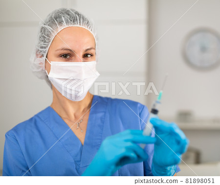 Nurse in a protective mask stands with a syringe filled with medicine Nurse in a protective mask stands with a syringe filled with medicine 81898051