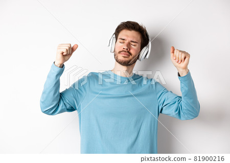Happy handsome man dancing to music in headphones, listening songs and smiling, standing over white background Happy handsome man dancing to music in headphones, listening songs and smiling, standing over white background 81900216