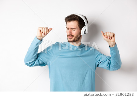 Happy young man having fun in headphones, dancing while listening music in wireless earphones, white background Happy young man having fun in headphones, dancing while listening music in wireless earphones, white background 81901288
