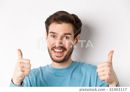 Close-up of cheerful man say yes, showing thumbs up in approval, praise good job, smiling approvingly, standing on white background Close-up of cheerful man say yes, showing thumbs up in approval, praise good job, smiling approvingly, standing on white background 81903117