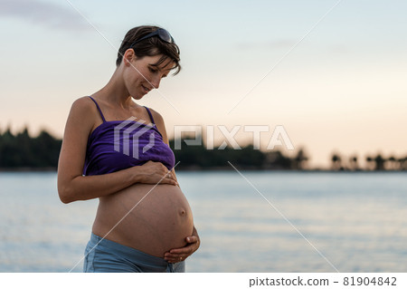 Young pregnant woman standing by the sea at dusk 81904842