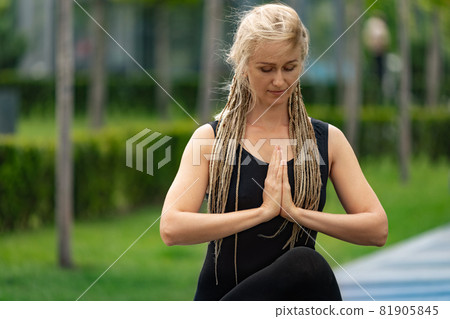 Close-up shot of beautiful woman with blonde hair doing yoga exercise in green public park in summer morning, outdoors. Healthy lifestyle, mental health concept. 81905845