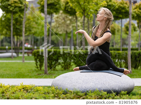 Young beautiful woman with blonde hair doing yoga exercise in green public park in summer morning, outdoors. Healthy lifestyle, mental health concept. 81905876
