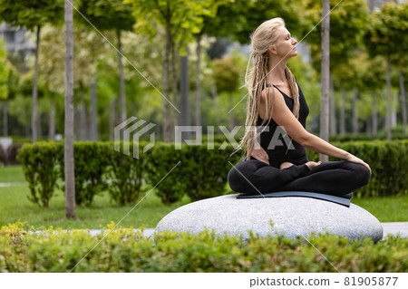 Young beautiful woman with blonde hair doing yoga exercise in green public park in summer morning, outdoors. Healthy lifestyle, mental health concept. Young beautiful woman with blonde hair doing yoga exercise in green public park in summer morning, outdoors. Healthy lifestyle, mental health concept. 81905877