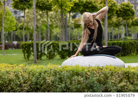 Young beautiful woman with blonde hair doing yoga exercise in green public park in summer morning, outdoors. Healthy lifestyle, mental health concept. Young beautiful woman with blonde hair doing yoga exercise in green public park in summer morning, outdoors. Healthy lifestyle, mental health concept. 81905879