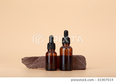 Two skin serum bottles next to natural stone against beige background with copy space 81907014