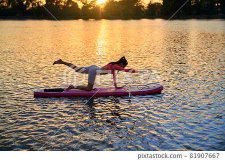 Woman practicing yoga on sup board during summer sunset 81907667