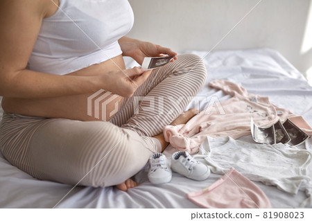 Top view of pregnant woman in the bed preparing baby clothes at home 81908023