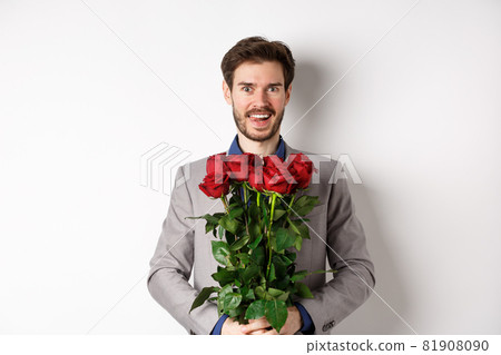 Excited handsome man in suit holding bouquet of roses for romantic date with lover, standing happy on Valentines day, white background Excited handsome man in suit holding bouquet of roses for romantic date with lover, standing happy on Valentines day, white background 81908090