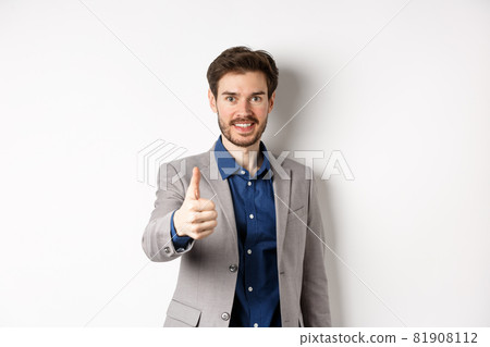Image of handsome businessman in suit showing thumb up and smiling, standing on white background 81908112