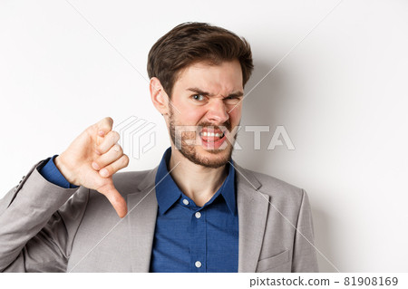 Close-up of disgusted guy in suit grimacing upset, showing thumbs down, express negative emotion, white background 81908169