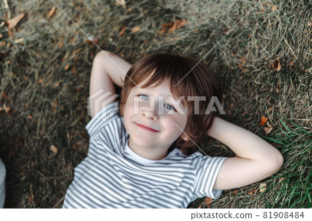 Kid lying on his back in the grass in park. Boy chilling on green lawn. Child relaxing outside, resting his head on garden meadow Kid lying on his back in the grass in park. Boy chilling on green lawn. Child relaxing outside, resting his head on garden meadow 81908484