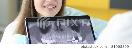 Portrait of smiling woman at dentist appointment holding tablet with an X-ray image of jaw Portrait of smiling woman at dentist appointment holding tablet with an X-ray image of jaw 81908809