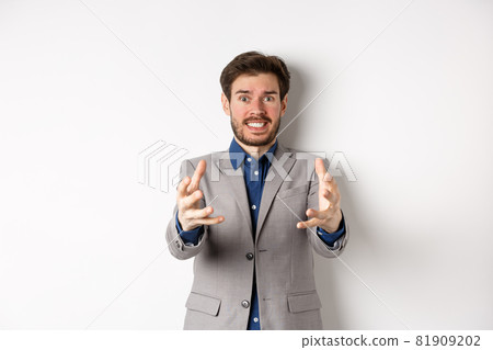 Distressed businessman stretch out hands to strangle annoying person, standing annoyed and frustrated against white background, wearing suit Distressed businessman stretch out hands to strangle annoying person, standing annoyed and frustrated against white background, wearing suit 81909202