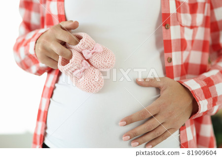 Pregnant woman holds pink slippers for newborn Pregnant woman holds pink slippers for newborn 81909604