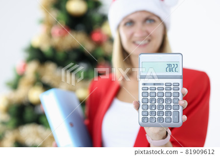 Woman accountant in santa claus hat holds calculator on background of christmas tree Woman accountant in santa claus hat holds calculator on background of christmas tree 81909612