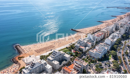 Beautiful aerial cityscapes of the tourist Portuguese city of Quarteira. On the seashore during the beach season with tourists who are sunbathing. 81910080