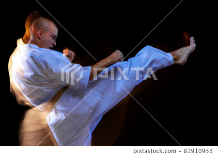 Side view cropped portrait of young karate sportsman training isolated over black background. Mixed light effect Side view cropped portrait of young karate sportsman training isolated over black background. Mixed light effect 81910933