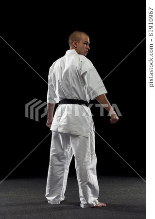 Back view full-length portrait of male sportsman in white kimono with black belt isolated over dark background Back view full-length portrait of male sportsman in white kimono with black belt isolated over dark background 81910967