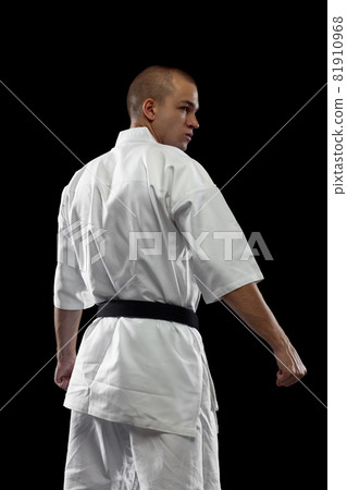 Back view. Cropped portrait of male sportsman in white kimono with black belt isolated over dark background Back view. Cropped portrait of male sportsman in white kimono with black belt isolated over dark background 81910968