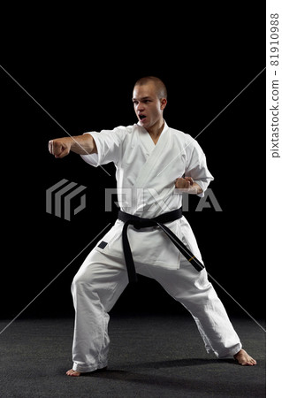 Full-length portrait of young sportsman training karate isolated over black background. Straight punch pose Full-length portrait of young sportsman training karate isolated over black background. Straight punch pose 81910988