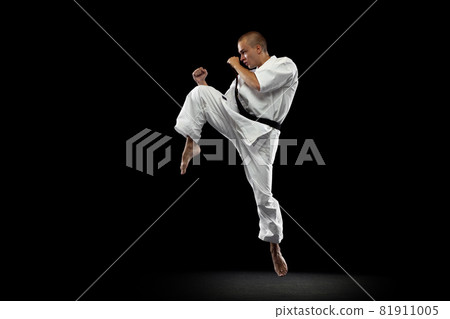 Full-length portrait of young sportsman training karate isolated over black background. In motion 81911005
