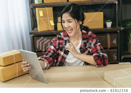 Asian woman startup small business at home office. Online seller entrepreneur young asian woman use tablet checking online order. Woman using tablet check stock goods supply delivery package shipping 81912158