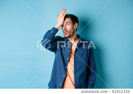 Annoyed man making facepalm and roll eyes from something stupid, standing over blue background with hand on forehead 81912320