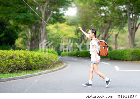 A girl carrying a school bag with her hands raised and crossing the road 81912837