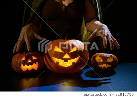 Close-up of female hands on a pumpkin for halloween in a dark studio. The witch is holding a jack-o-lantern 81913796
