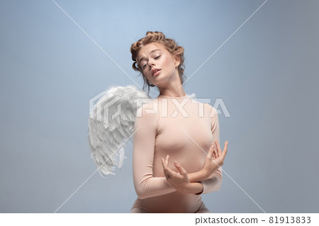 Portrait of pretty, slim beautiful young girl, graceful ballerina in image of angel with wings sitting on cloud isolated on white gray studio background. 81913833