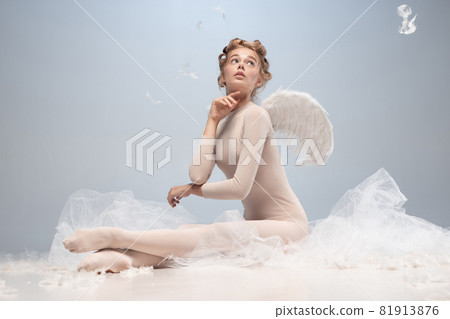 Portrait of pretty, slim beautiful young girl, graceful ballerina in image of angel with wings sitting on cloud isolated on white gray studio background. Portrait of pretty, slim beautiful young girl, graceful ballerina in image of angel with wings sitting on cloud isolated on white gray studio background. 81913876