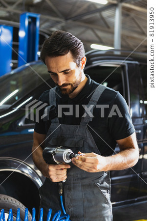 Portrait of young man, male auto mechanic in dungarees working at car service station, indoors. Concept of labor, occupation, business, caree, job 81913950