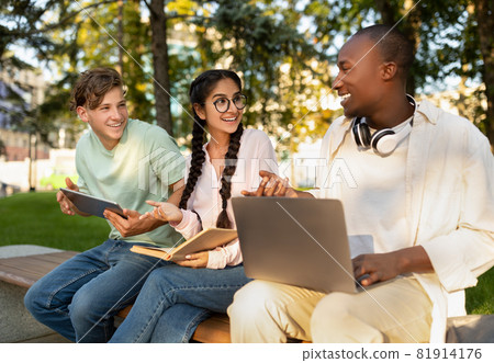 Students lifestyle. Three university friends learning together, using laptops and reading book, sitting in campus Students lifestyle. Three university friends learning together, using laptops and reading book, sitting in campus 81914176