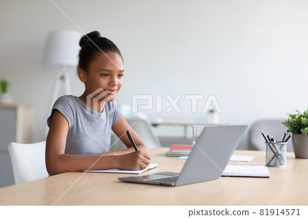 Smiling pretty smart teen african american girl student studying at home, watching online lesson on laptop Smiling pretty smart teen african american girl student studying at home, watching online lesson on laptop 81914571