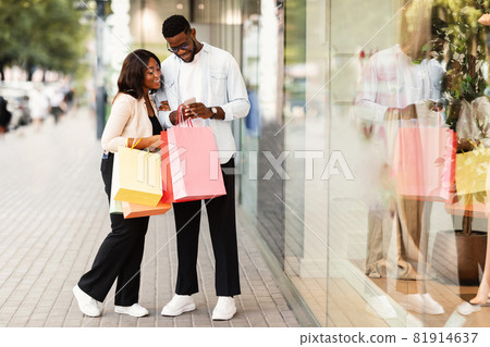 Happy black man and woman using phone holding shopping bags Happy black man and woman using phone holding shopping bags 81914637