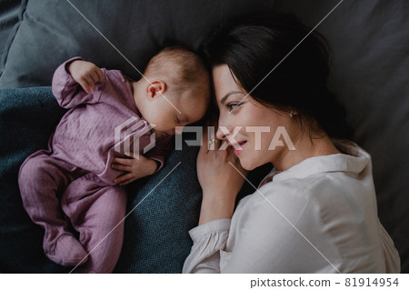 Top view of happy young mother with her newborn baby girl lying on sofa indoors at home. 81914954
