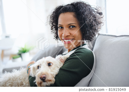 Portrait of happy mature woman with dog sitting indoors at home, looking at camera. 81915049