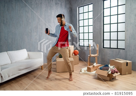 Happy young man with headphones dancing and celebrating moving home surrounded by packing boxes, new living concept. 81915095