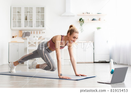 Smiling caucasian cute young fitness female do leg exercises and watch online workout on laptop at home 81915453