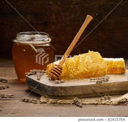 wax honeycomb with honey on a wooden board, behind a jar of honey 81915764