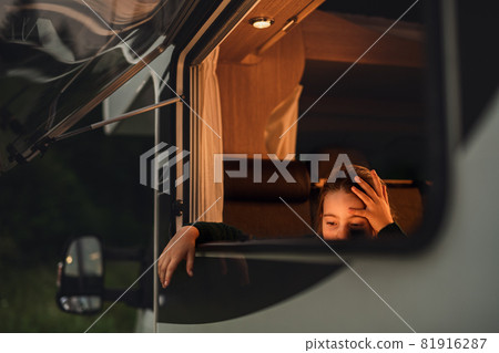 Sad small girl by caravan window at dusk, family holiday trip. 81916287