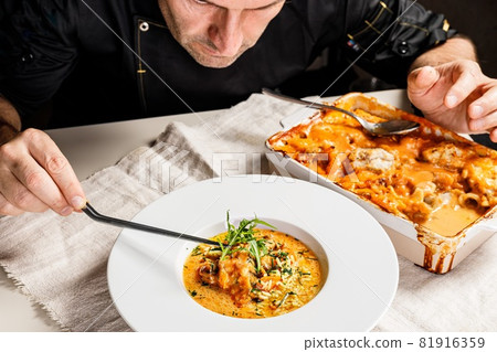 Authentic Spanish paella with cod and mussels. Traditional Mediterranean seafood dish. The chef decorates the dish with herbs using tweezers. Restaurant dish serving. People at work. 81916359